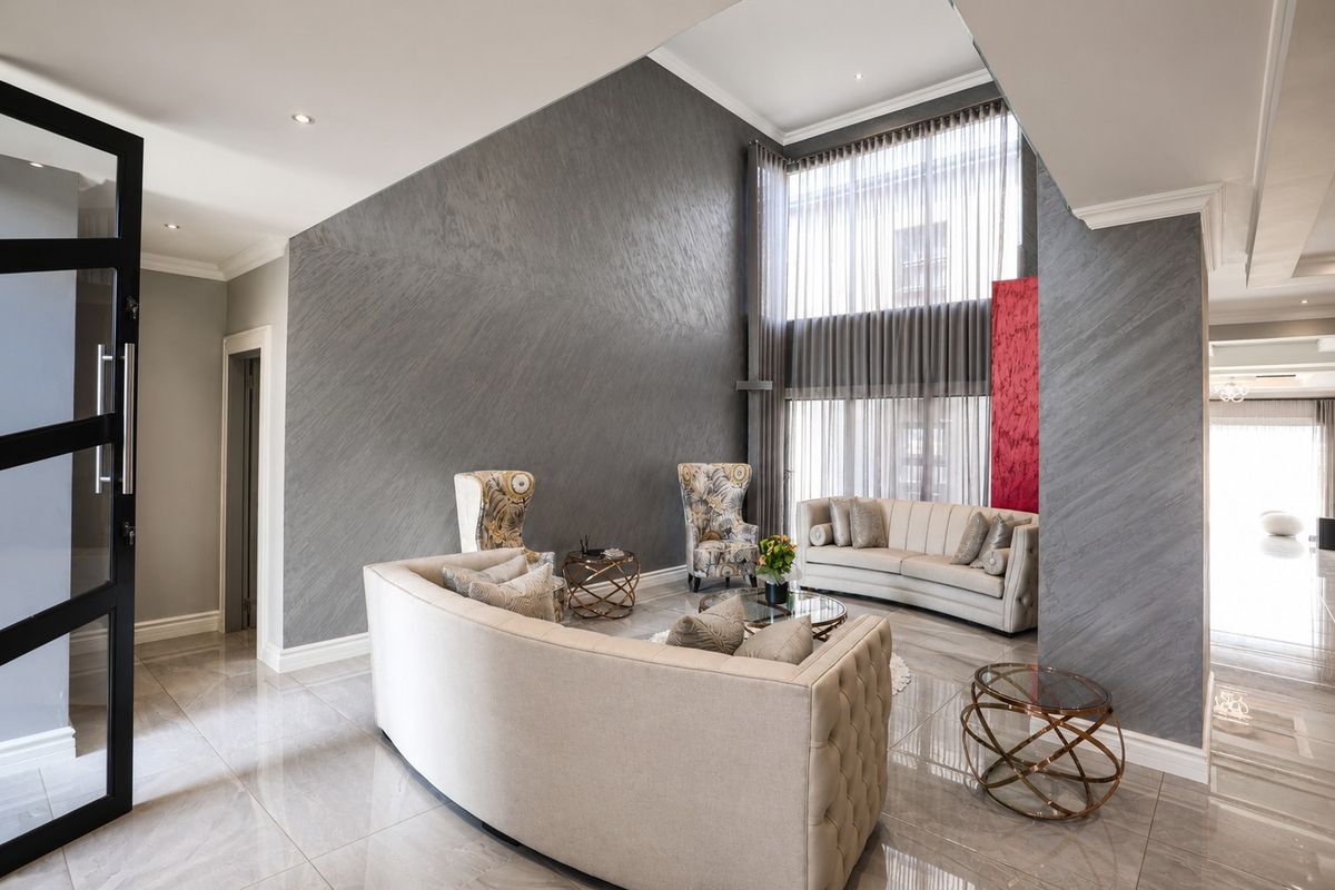 Spacious double-volume living room featuring high ceilings, large floor-to-ceiling windows, elegant textured feature walls, and polished porcelain floor tiles.