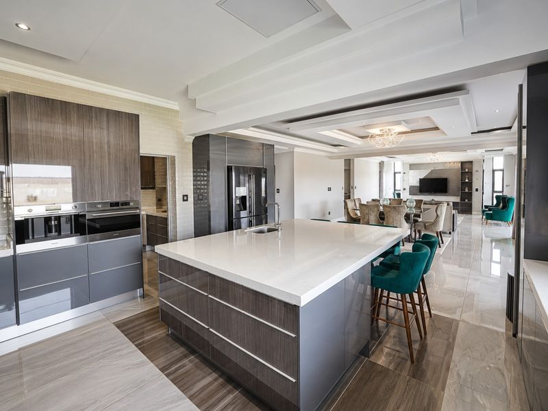 Modern open-plan kitchen featuring a large island with quartz countertops, high-end built-in appliances, and elegant coffered ceilings, flowing seamlessly into the living and dining area.