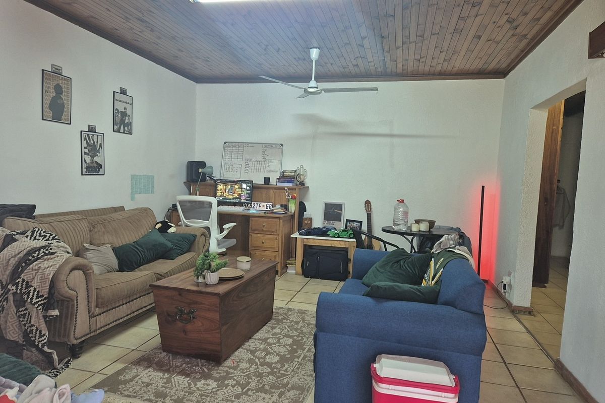 A living room featuring a timber-clad ceiling, ceiling fan, and ceramic floor tiles, offering a functional space for relaxation and home office use.
