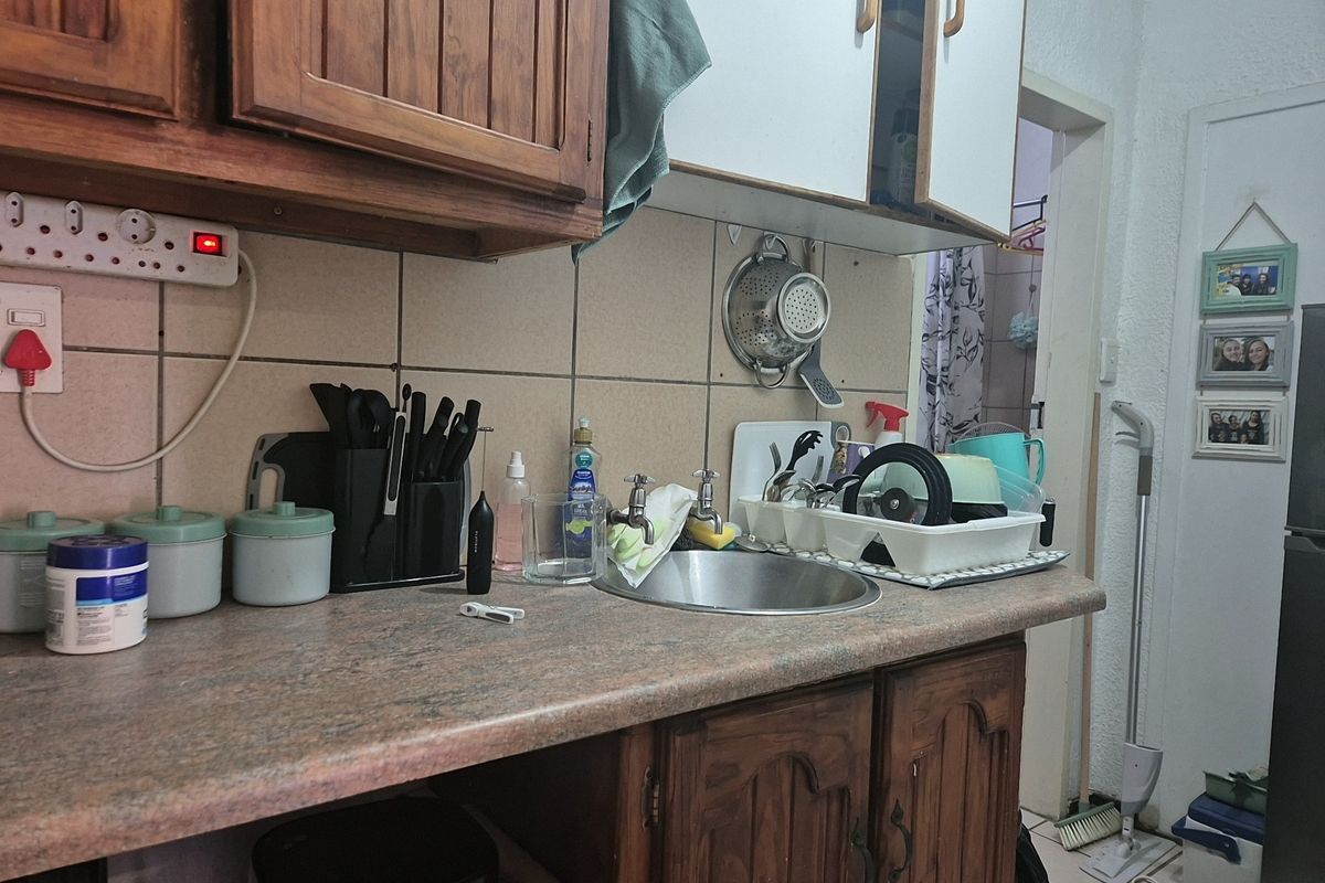 A compact kitchen area featuring wooden cabinetry, a laminate countertop, and a stainless steel sink with a tiled backsplash.
