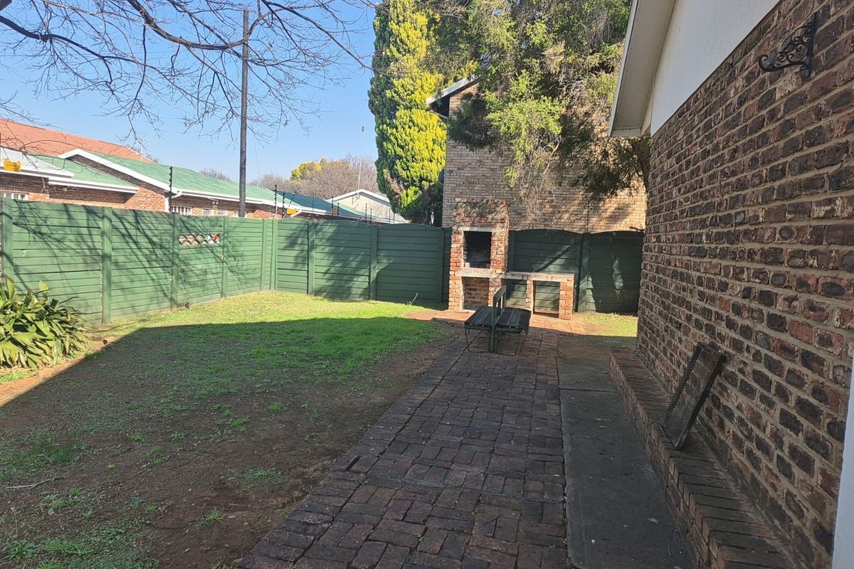 A private rear garden featuring a brick-paved patio area, a built-in braai, and perimeter fencing, offering potential for outdoor entertainment.