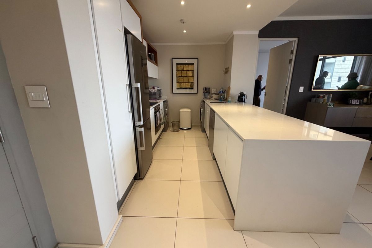 Modern kitchen featuring a large central island, sleek white cabinetry, stone countertops, and integrated appliances with clean tiled flooring.