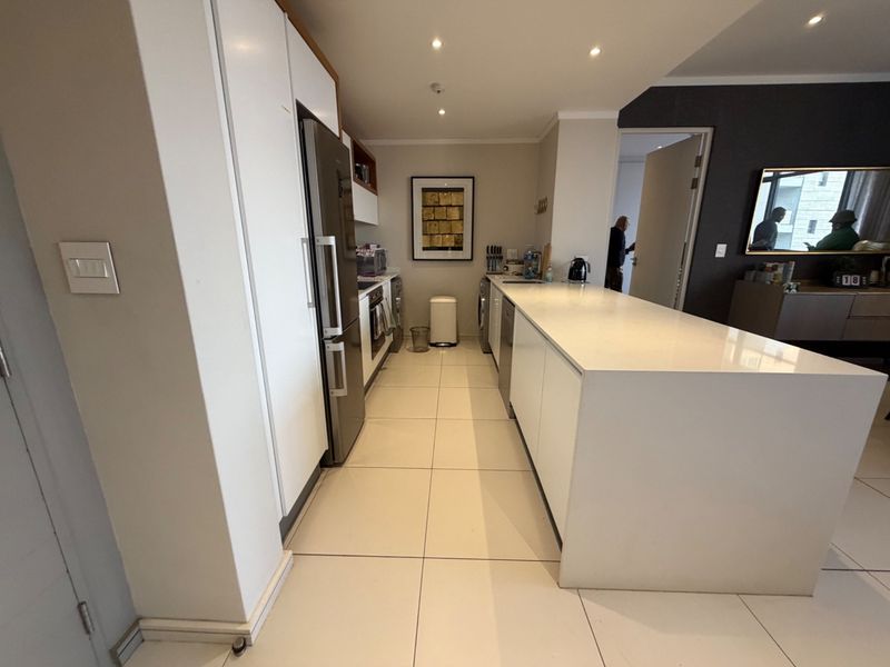 Modern kitchen featuring a large central island, sleek white cabinetry, stone countertops, and integrated appliances with clean tiled flooring.