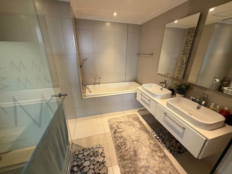 Modern bathroom featuring a double vanity with wall-mounted cabinetry, a built-in bathtub, and a separate glass-enclosed shower with neutral wall and floor tiling.
