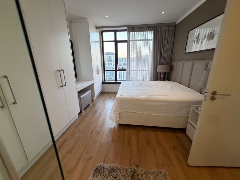 Modern bedroom featuring built-in cupboards, laminate flooring, and a large window with city views, creating a bright and comfortable living space.