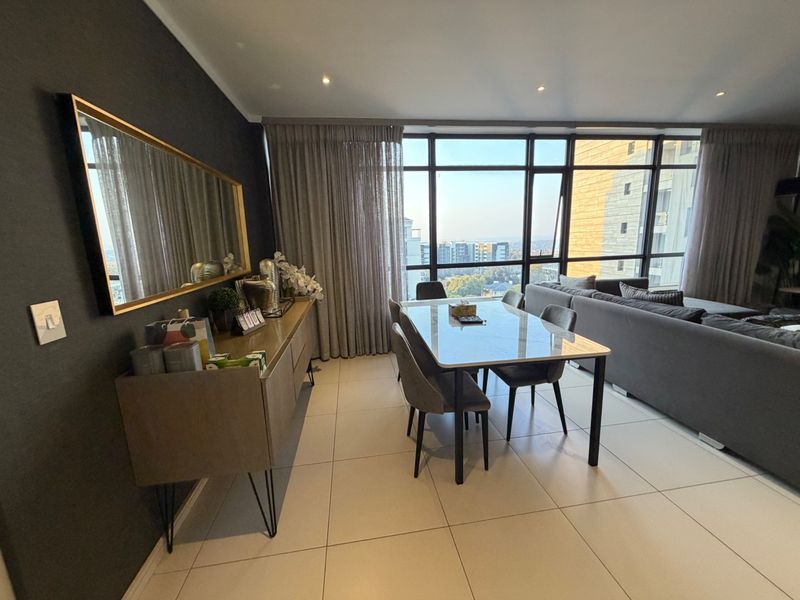 Modern open-plan living and dining area featuring large floor-to-ceiling windows with expansive city views and neutral tiled flooring.