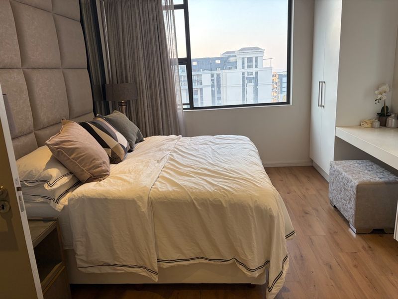 A well-maintained bedroom featuring laminate flooring, a large window with city views, and a built-in wardrobe with an integrated vanity area.