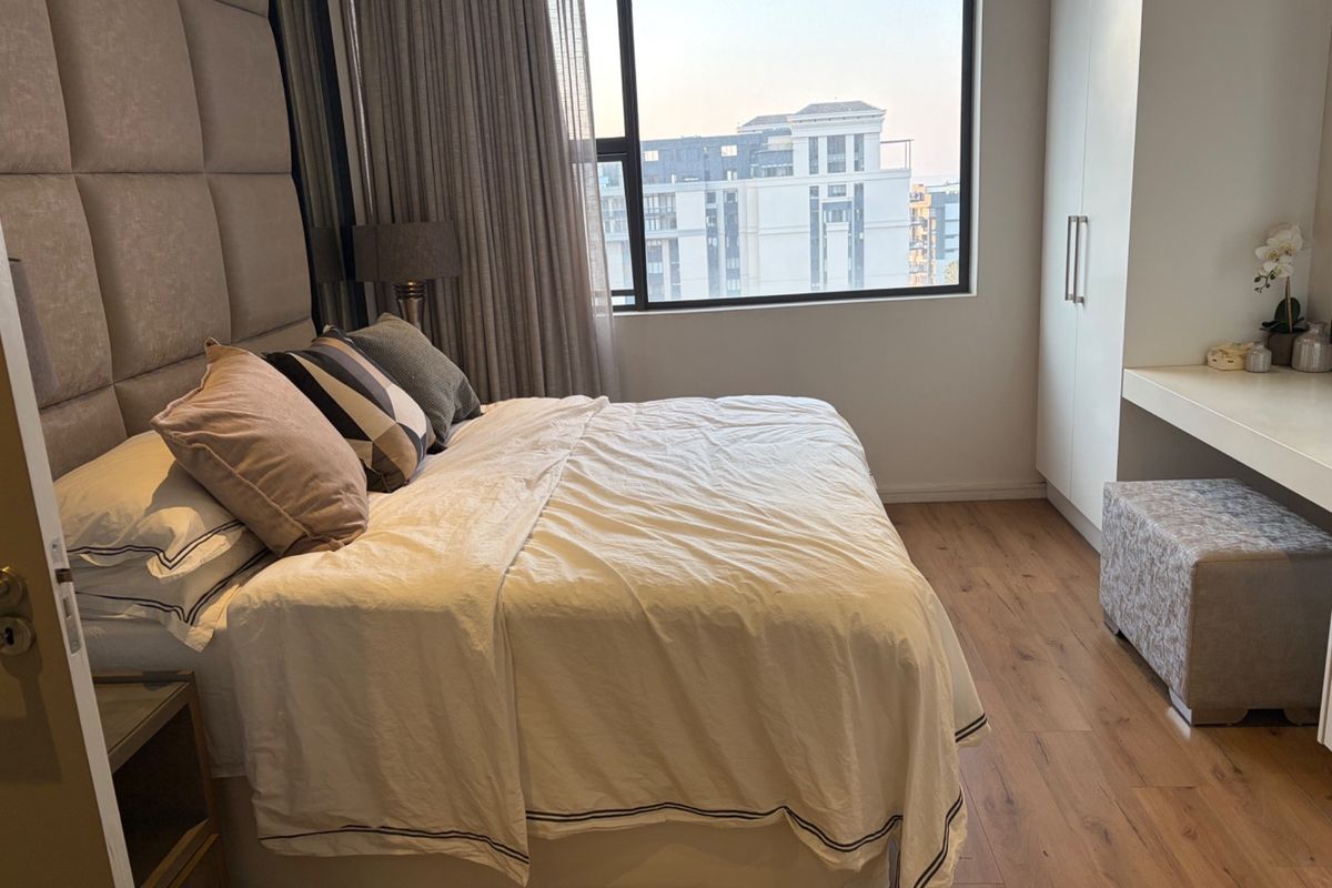 A well-maintained bedroom featuring laminate flooring, a large window with city views, and a built-in wardrobe with an integrated vanity area.