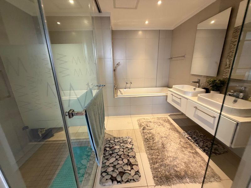 Modern bathroom featuring a double vanity, built-in bathtub, and a separate glass-enclosed shower with neutral tiling throughout.