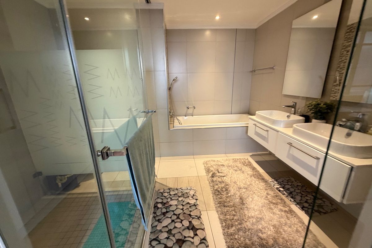 Modern bathroom featuring a double vanity, built-in bathtub, and a separate glass-enclosed shower with neutral tiling throughout.