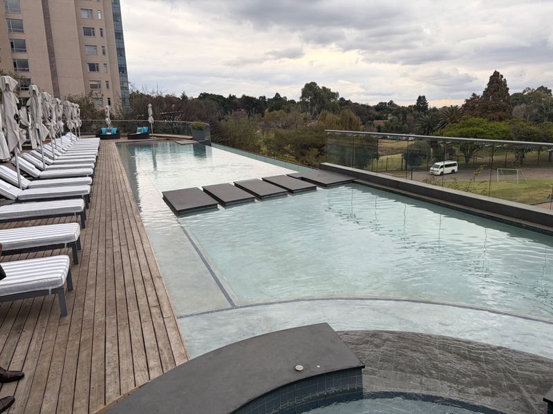 A modern infinity-edge swimming pool featuring timber decking and a glass balustrade, offering elevated views of the surrounding landscape.