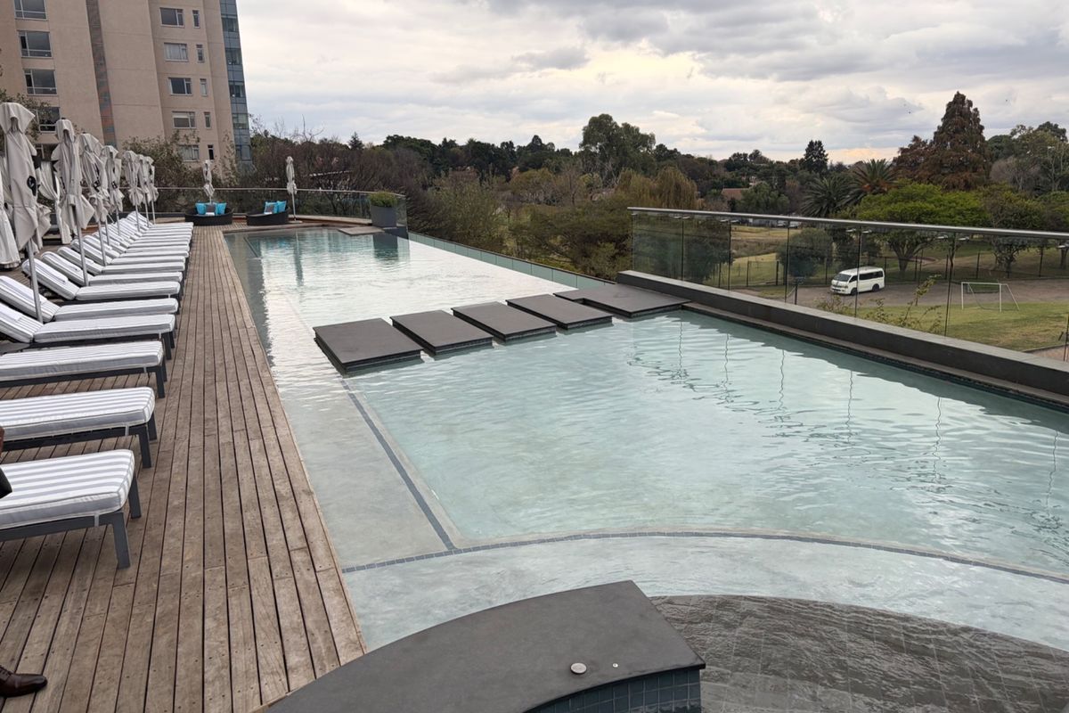 A modern infinity-edge swimming pool featuring timber decking and a glass balustrade, offering elevated views of the surrounding landscape.