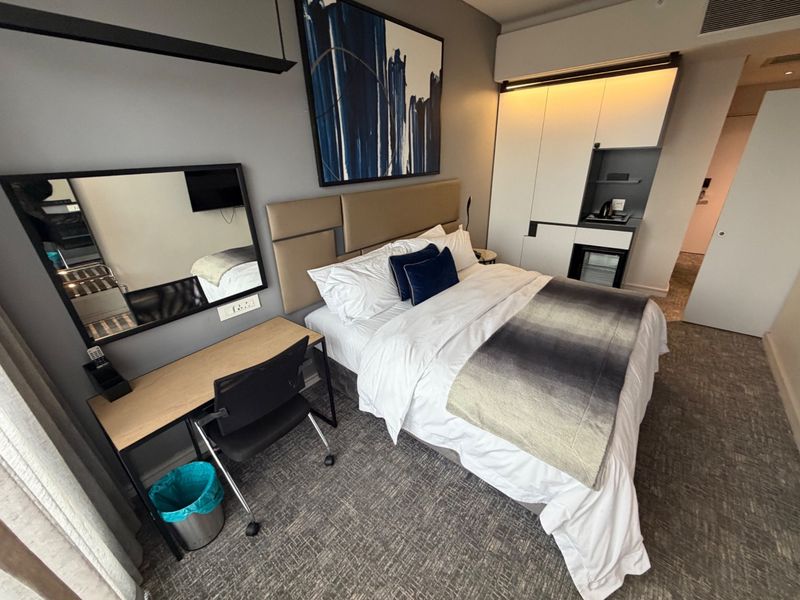 A modern bedroom featuring a built-in wardrobe with integrated lighting, neutral wall tones, and carpeted flooring.