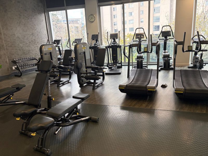 A well-equipped modern gym facility featuring professional-grade exercise machines, rubberized flooring, and large windows providing ample natural light.