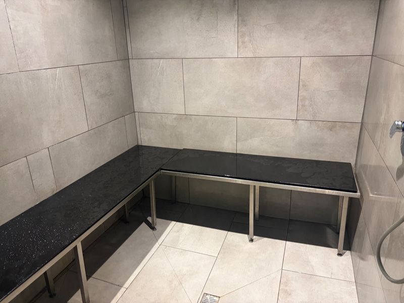 A modern, minimalist sauna featuring sleek large-format wall tiles, a built-in stone bench with a stainless steel frame, and a functional floor drain.