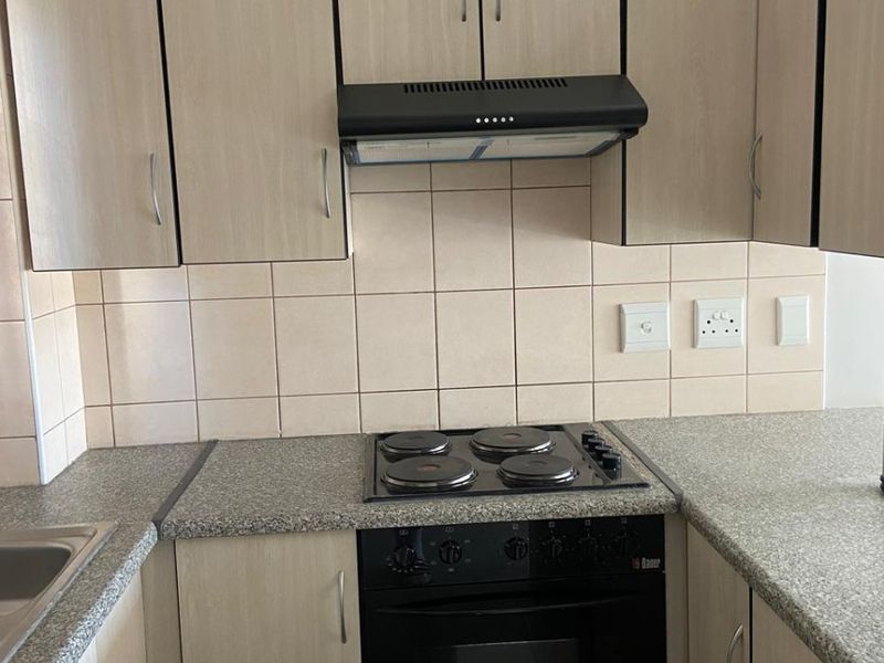 A functional kitchen featuring light wood-finish cabinetry, granite-look countertops, a built-in oven with hob, and a tiled backsplash.