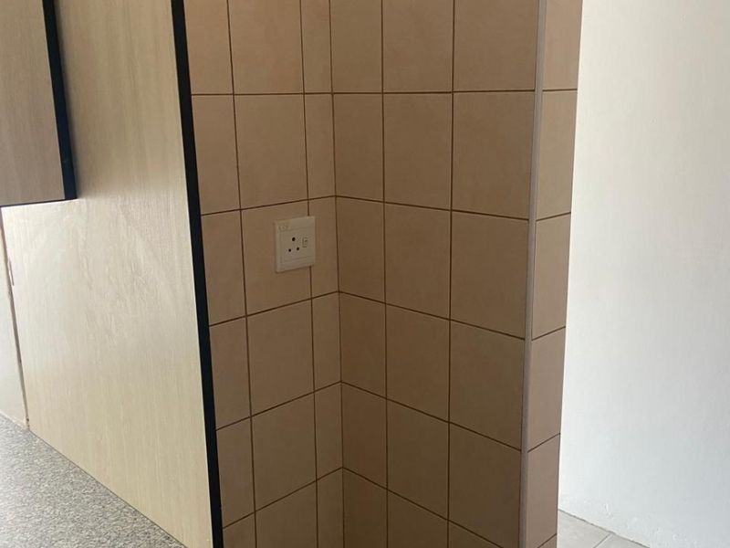 A clean kitchen corner featuring neutral tiled splashbacks, laminate cabinetry, and a durable countertop, providing a functional and well-maintained workspace.