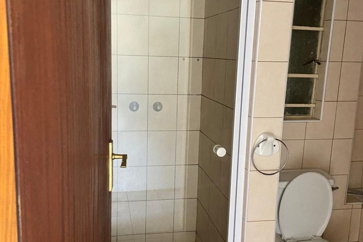 A functional bathroom featuring a shower enclosure, ceramic tiling, and a standard toilet, presenting a dated but well-maintained space ready for modernization.
