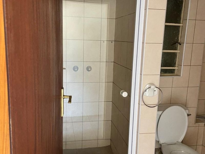 A functional bathroom featuring a shower enclosure, ceramic tiling, and a standard toilet, presenting a dated but well-maintained space ready for modernization.