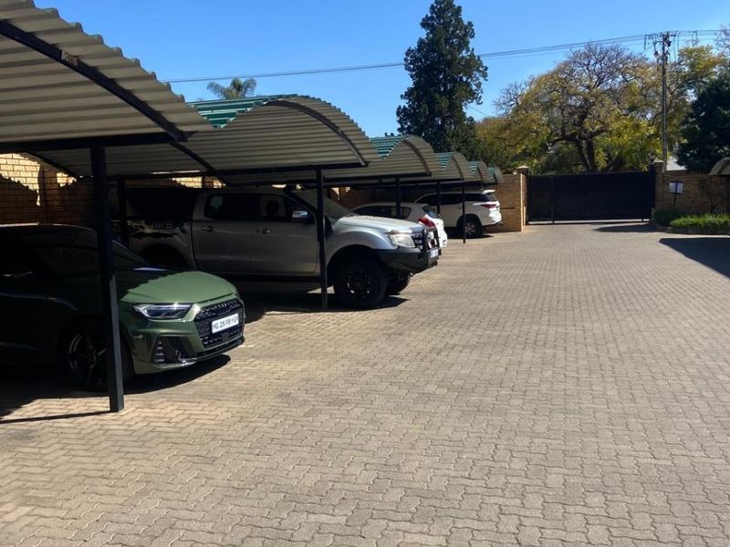 A paved outdoor parking area featuring multiple covered carport bays and a secure perimeter wall with a gated entrance.