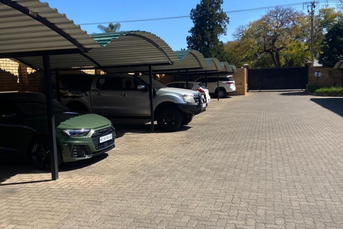 A paved outdoor parking area featuring multiple covered carport bays and a secure perimeter wall with a gated entrance.