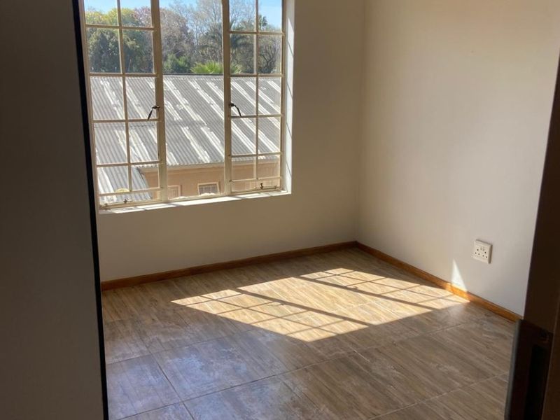 A bright, empty bedroom featuring wood-look tiled flooring and a large multi-pane window providing natural light.