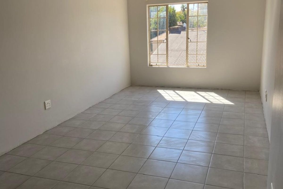 A bright, empty bedroom featuring neutral tiled flooring, a large window with security bars, and a simple ceiling-mounted spotlight fixture.