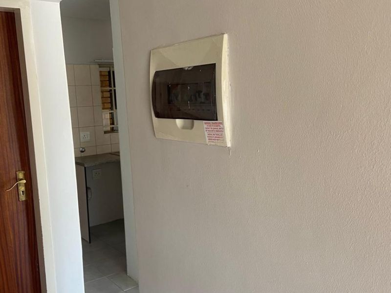 A view of a hallway featuring a wall-mounted electrical distribution board, with a glimpse into an adjacent tiled kitchen area.
