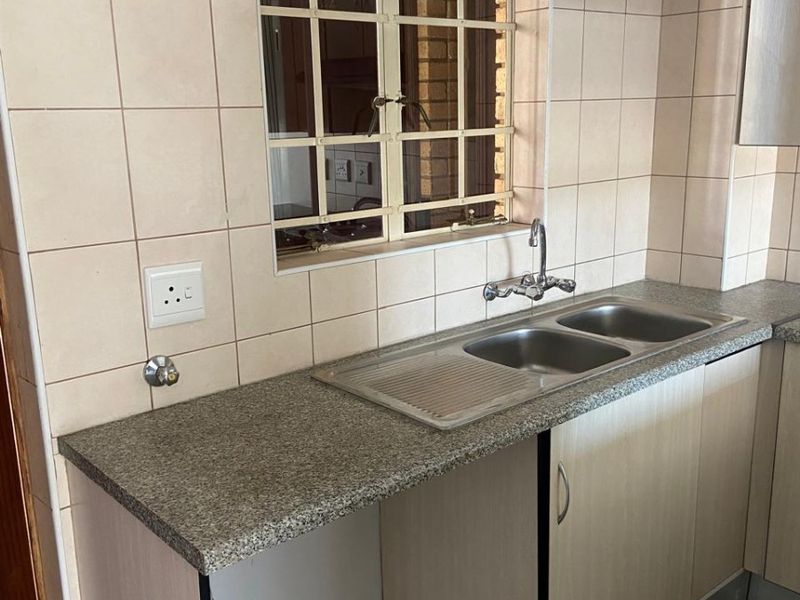 A functional kitchen area featuring a double bowl stainless steel sink, granite countertops, and tiled splashbacks with built-in cabinetry.