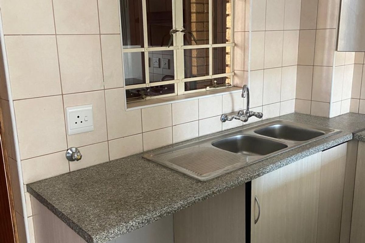 A functional kitchen area featuring a double bowl stainless steel sink, granite countertops, and tiled splashbacks with built-in cabinetry.