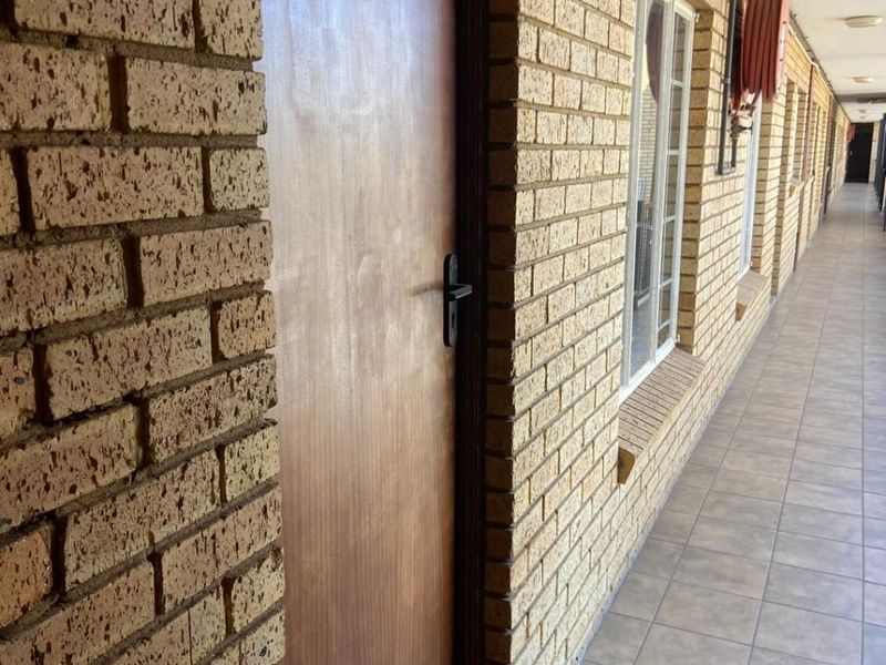 An exterior apartment hallway featuring brick walls, tiled flooring, and a numbered entrance door with a fire hose reel mounted on the wall.
