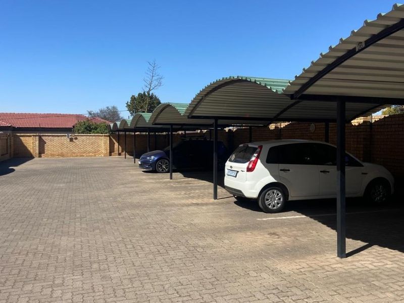 A paved outdoor parking area featuring multiple covered bays with corrugated metal roofing and secure brick boundary walls.