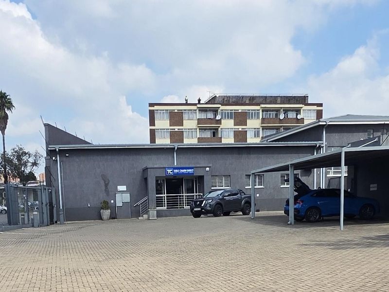 Commercial property exterior featuring a paved parking lot, covered parking bays, and a secure main entrance facade.