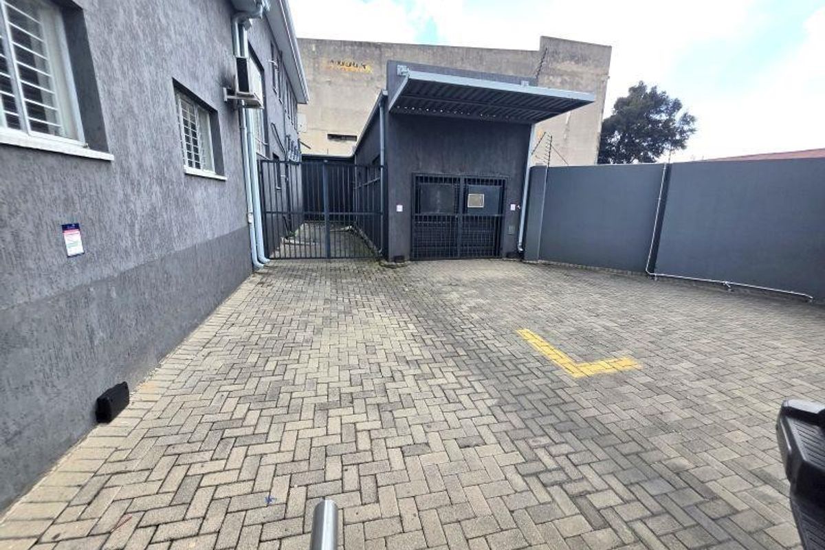 A paved rear exterior area featuring secure gated access, perimeter walling, and a metal awning structure.