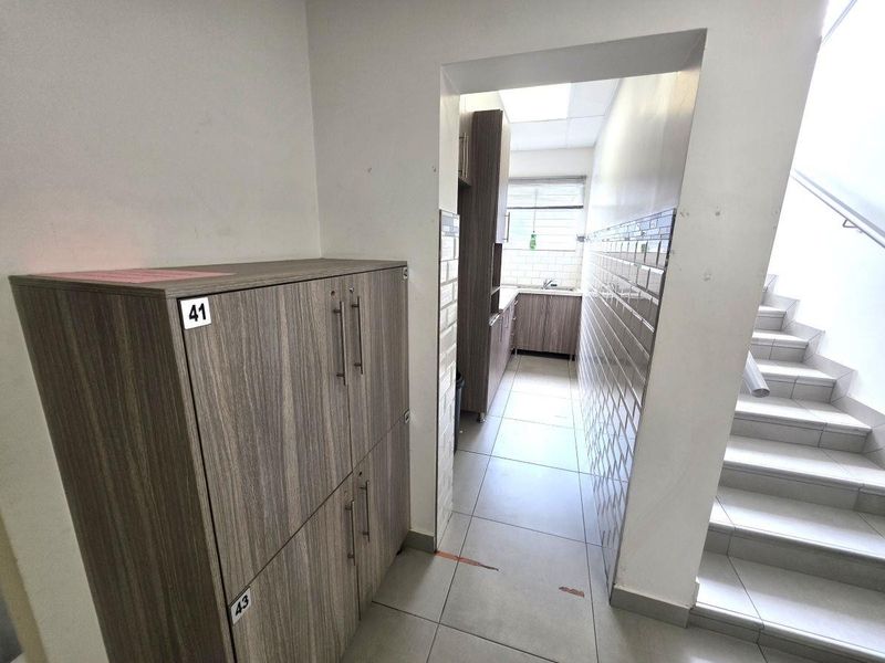 A functional hallway area featuring tiled flooring, subway tile wall accents, and access to a small kitchenette and staircase.