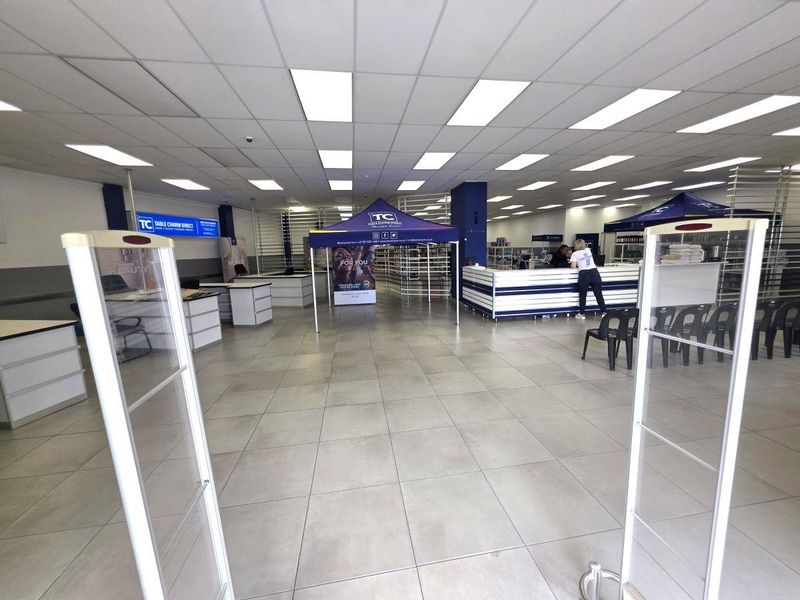 Spacious commercial open-plan retail area featuring neutral ceramic floor tiles, a suspended ceiling with recessed lighting, and integrated service counters.
