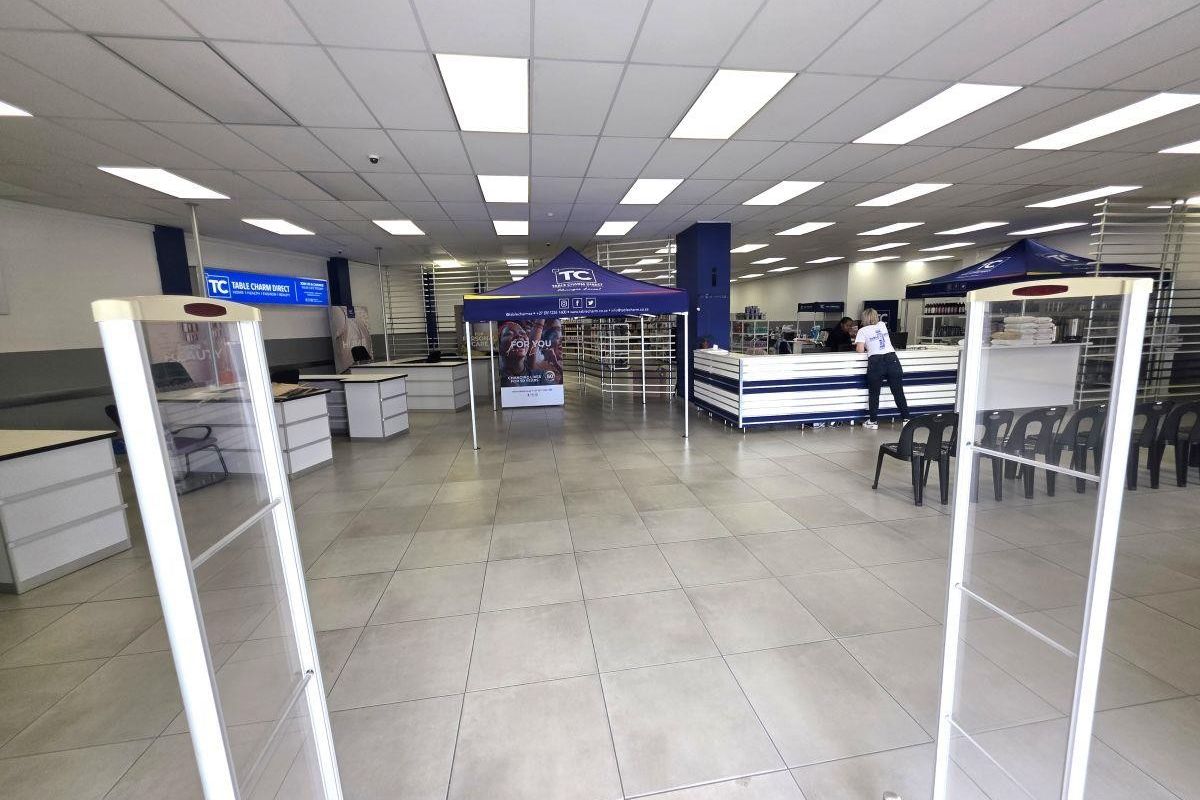 Spacious commercial open-plan retail area featuring neutral ceramic floor tiles, a suspended ceiling with recessed lighting, and integrated service counters.