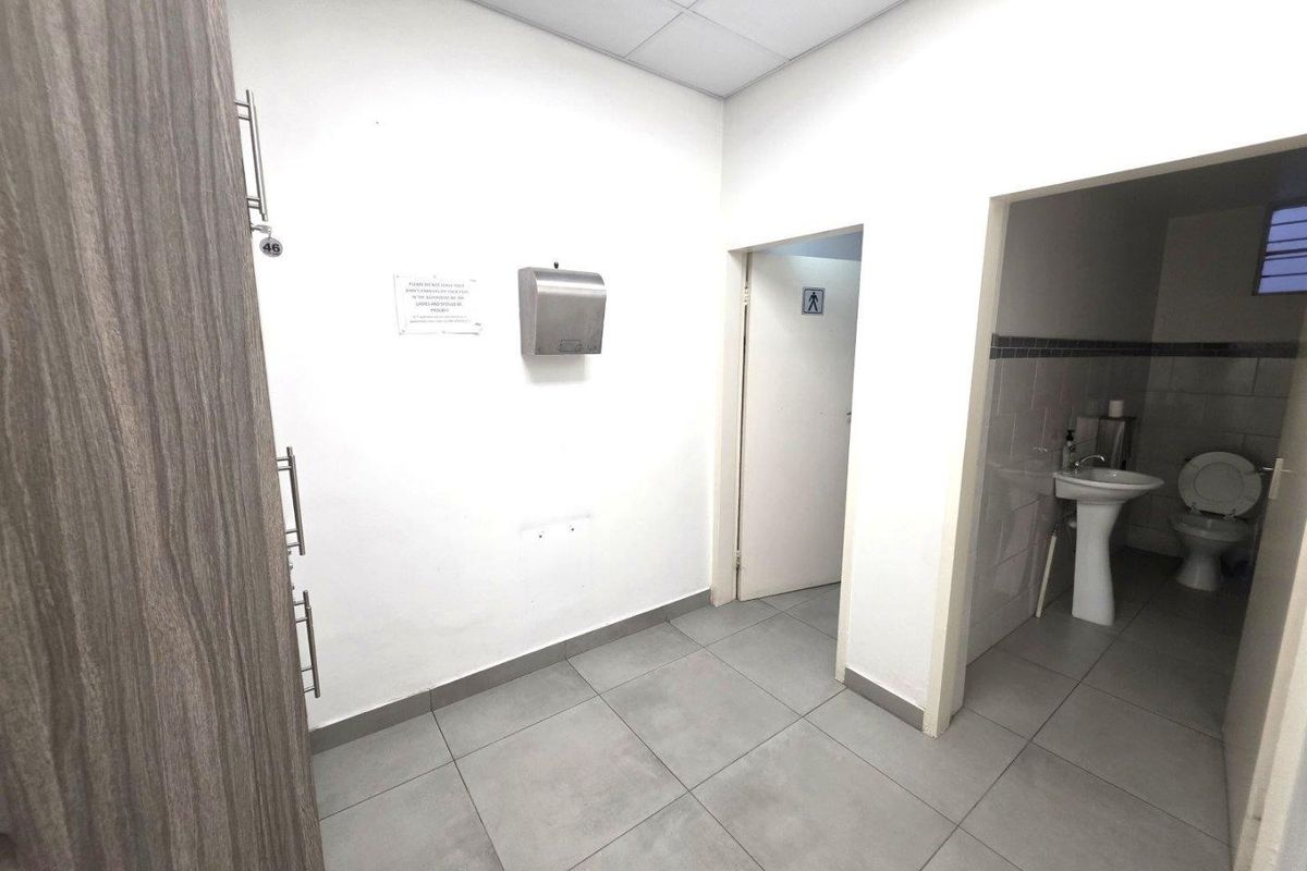 A functional commercial restroom area featuring tiled flooring, a pedestal sink, and a toilet, with a neutral white finish.