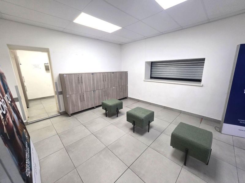 A functional utility or locker room featuring built-in storage lockers, tiled flooring, and a security roller shutter over the window.