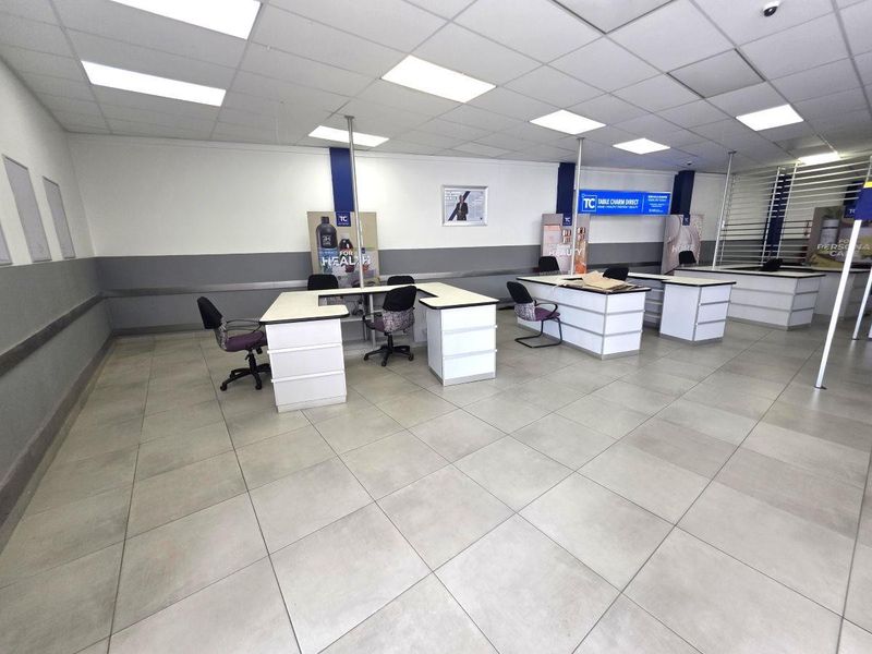 A commercial office space featuring a suspended ceiling, recessed lighting, and durable ceramic floor tiles with integrated built-in desk units.