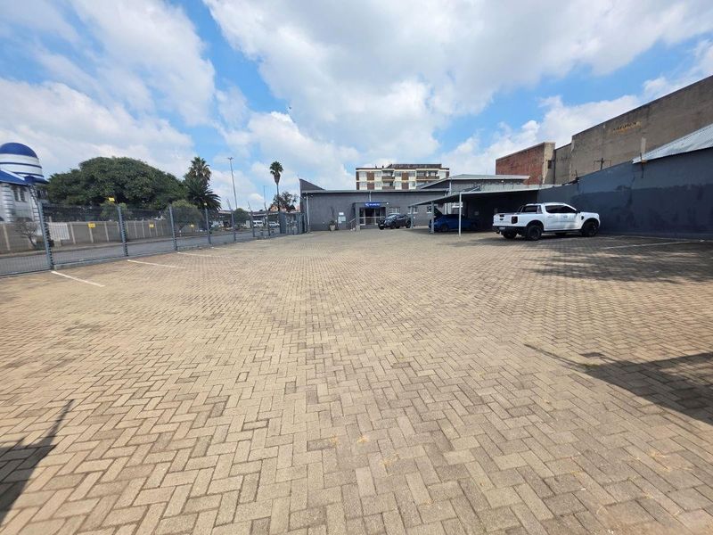 Spacious paved commercial parking area featuring covered parking bays and secure perimeter fencing, providing ample space for vehicles.