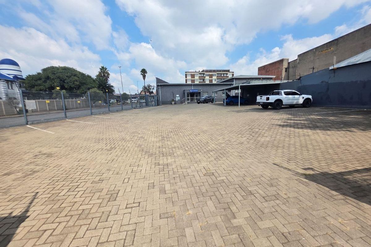 Spacious paved commercial parking area featuring covered parking bays and secure perimeter fencing, providing ample space for vehicles.