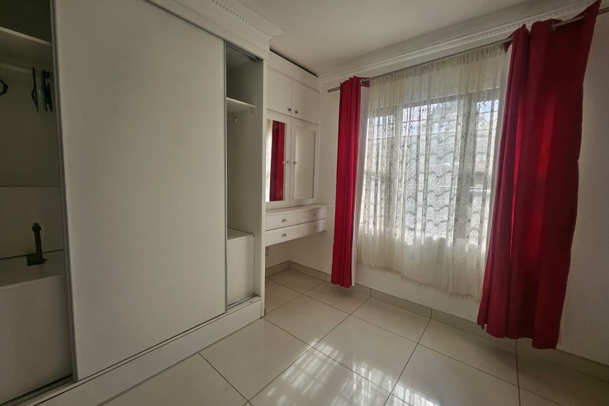 A bright bedroom featuring tiled flooring, built-in cupboards with an integrated vanity unit, and large windows with decorative curtains.