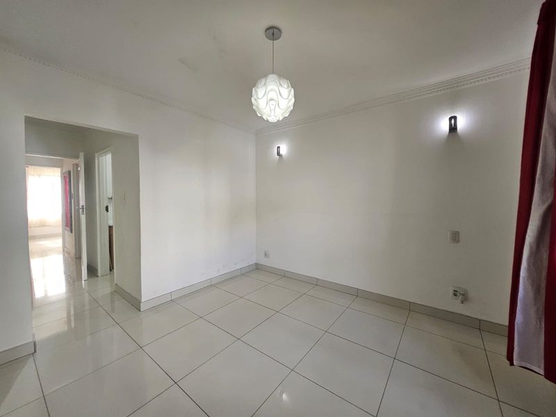 A bright, empty living room featuring neutral ceramic floor tiles, coved ceiling cornices, and modern wall-mounted lighting fixtures.