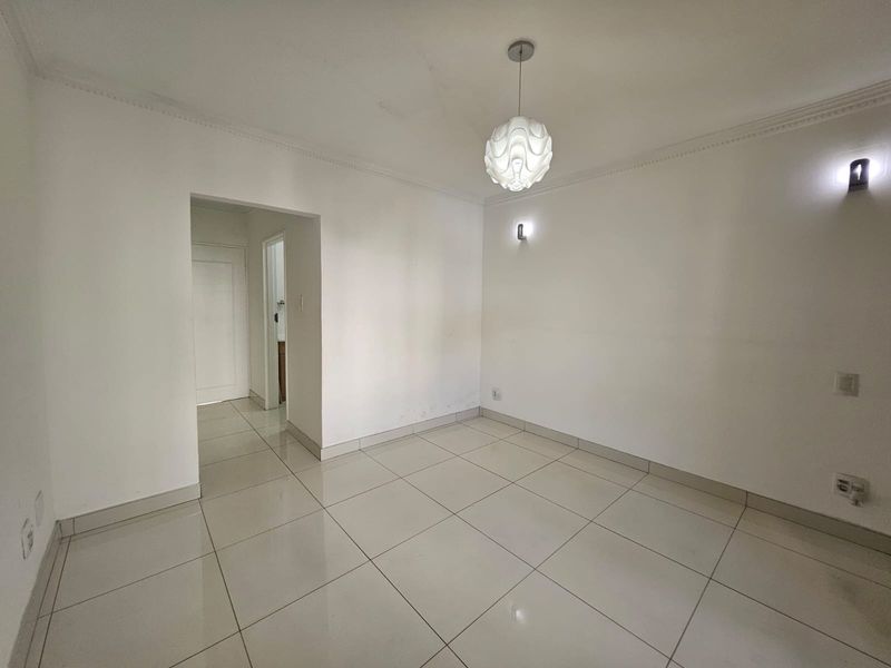 An empty, neutrally finished living area featuring tiled flooring, decorative cove cornicing, and modern wall-mounted lighting.