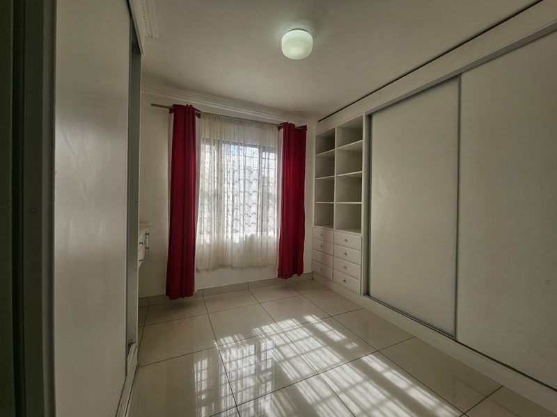 A bright, empty bedroom featuring tiled flooring, extensive built-in storage with sliding doors, and a window with natural light.