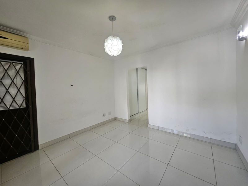 An empty living area featuring tiled flooring, a wall-mounted air conditioner, and a security gate, leading into a space with built-in storage.