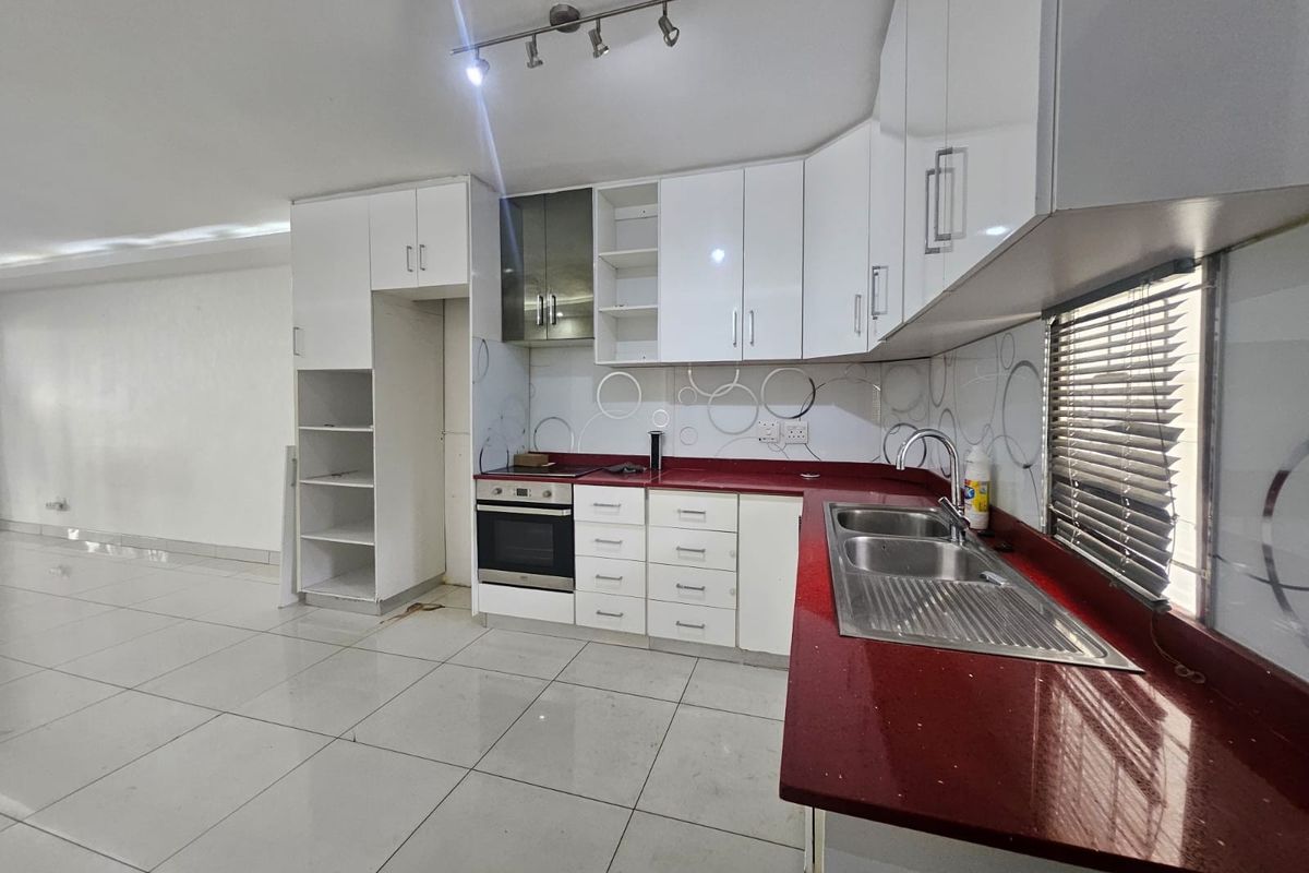 A functional kitchen featuring white cabinetry, a bold red countertop, built-in oven, and tiled flooring, offering a clean canvas for modern updates.