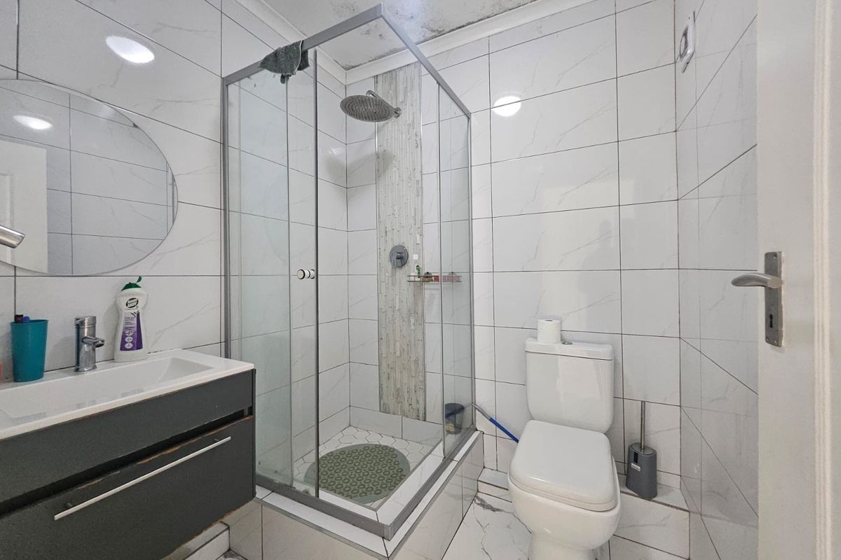 A compact bathroom featuring a glass shower enclosure, modern vanity, and white tiled finishes, currently showing signs of ceiling water damage.