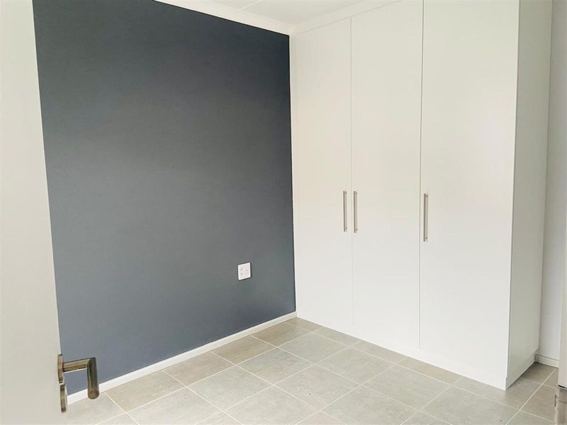 A clean, empty bedroom featuring modern tiled flooring, a dark accent wall, and white built-in cupboards providing ample storage space.